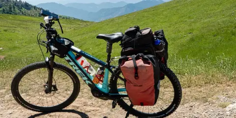 Bereit für e bike touren: Ein Trek E-Bike mit Gepäcktaschen steht auf einem Schotterweg, umgeben von grünen Hügeln und Bergketten.