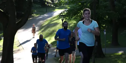 En grupp löpare i en park, en kvinna i ljusblå tröja springer framåt. Kanske undrar du vad betyder anaerob träning när du ser dem kämpa uppför backen.