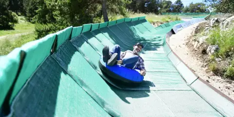 Un homme souriant dévale une piste verte en luge gonflable, profitant des activités Mont Ventoux.