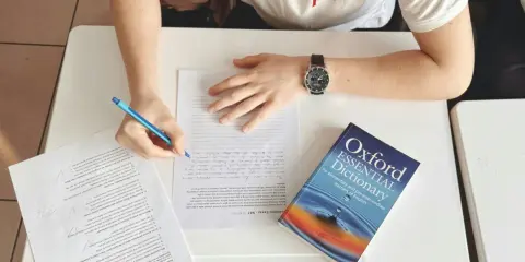 Uczeń pisze wypracowanie, a obok leży słownik "Oxford Essential Dictionary". Zastanawia się, co to jest "suffix" i jak go użyć.