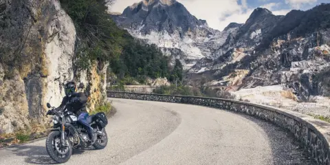 Motociclista su strada tortuosa con montagne di marmo sullo sfondo, un'autentica **Toscana da visitare**.