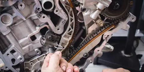 Mechanik naprawia rozrząd silnika. Luźny łańcuch może być jednym z objawów zużytej poduszki silnika.