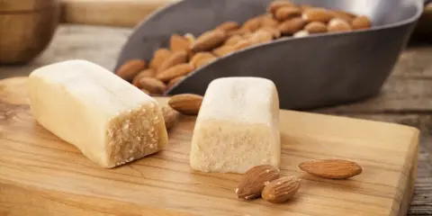 Deux blocs de pâte d'amande et des amandes dans une pelle, prêts pour une recette de pâte d'amande maison.