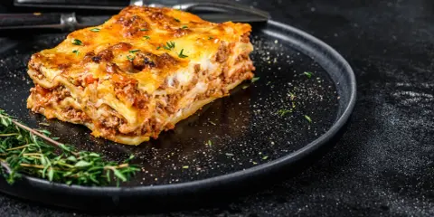En bit gyllene lasagne på en svart tallrik, perfekt comfort food med köttfärs och ost.