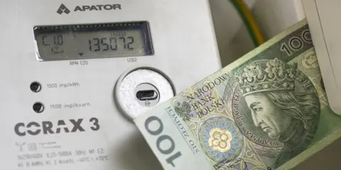 Licznik energii elektrycznej z banknotem 100 zł. Wysokie rachunki za prąd to problem, ale dodatek energetyczny może pomóc.