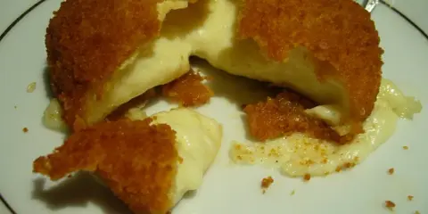 Złocisty camembert w panierce z rozpływającym się, kremowym wnętrzem na białym talerzu.