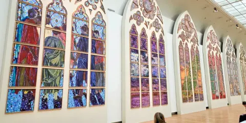 Des vitraux contemporains de Notre-Dame, des œuvres vibrantes composées de multiples panneaux peints, évoquant des scènes humaines et des paysages colorés.