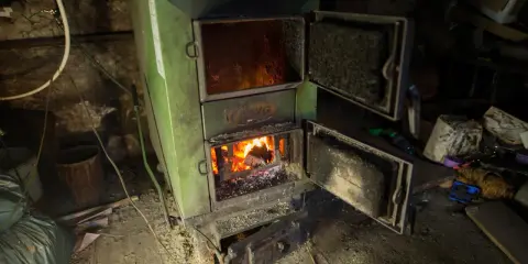 Zielony piec z otwartymi drzwiczkami, w którym pali się ogień. Pytanie o kotły klasy 1 do kiedy jest ważne dla ogrzewania domu.