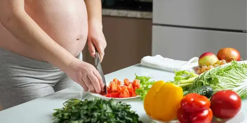 Schwangere bereitet gesunde Mahlzeit zu. Bunte Paprika, Tomaten und frisches Gemüse für eine gute Ernährung während der Schwangerschaft.