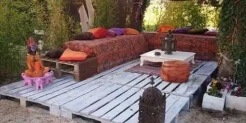 Un rincón zen con sofás y mesas bajas creados con jardineras con palets, cojines coloridos y faroles.
