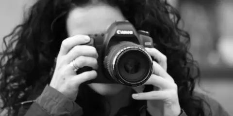 Czarno-białe zdjęcie kobiety z kręconymi włosami, która trzyma aparat Canon. To jej pierwsze szkolenie z fotografii.