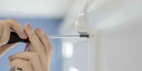 Montaż rolet okiennych z prowadnicami. Ręce przykręcają śrubę w uchwycie prowadnicy.