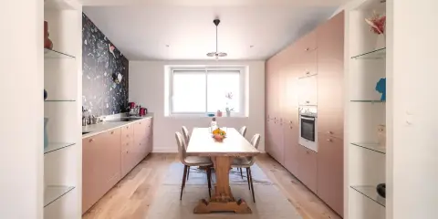 Une cuisine salle à manger et salon dans la même pièce, avec des meubles roses, un papier peint floral et une table en bois.
