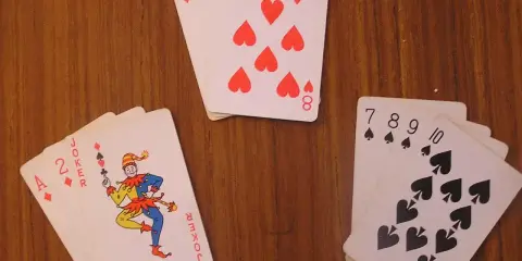 Karty na drewnianym stole: as, dwójka, joker i inne. Joker w kartach wygląda jak wesoły błazen.