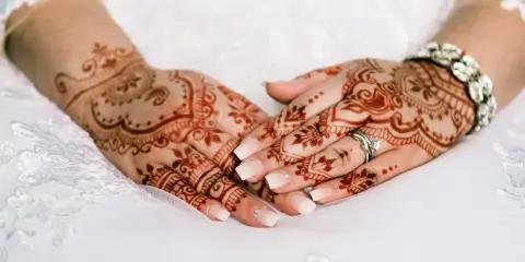 Manos de novia con intrincados diseños de henna, anillos y pulsera brillante, listas para la boda.