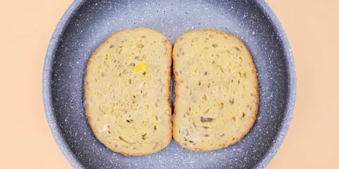 Dwa kawałki chleba w jajku smażą się na patelni.
