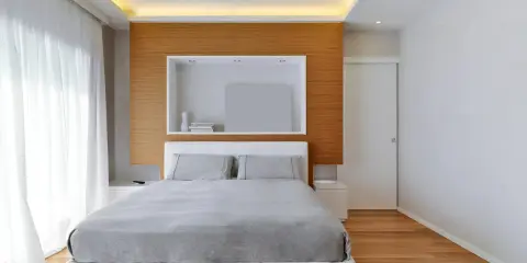 Illuminazione a scomparsa nel controsoffitto, un'idea moderna per un soffitto elegante. Camera da letto minimalista con letto bianco e testiera in legno.