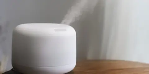 Humidificador casero blanco emitiendo vapor sobre una mesa de madera.