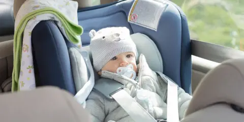 Bebé con gorro de oso y chupete en un alzador o silla coche, listo para un viaje seguro.