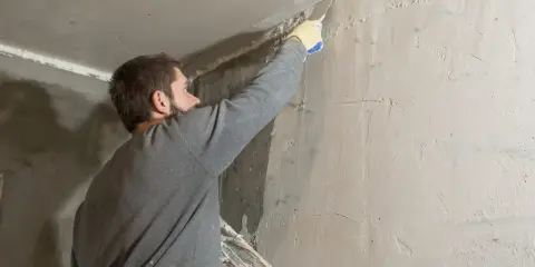 Hombre aplicando masilla en una esquina para quitar el gotele del techo.