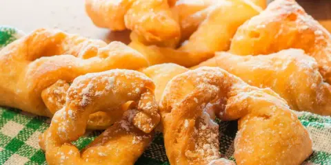 Beignets dorés saupoudrés de sucre glace sur un torchon à carreaux verts.