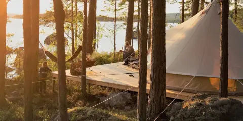 Kloten Nature Resort: en man sitter på en altan vid en sjö, bredvid ett stort tält. En hängmatta och en eldskål syns också.