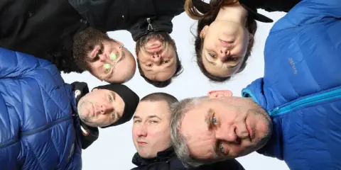 Grupa ludzi, w tym jeden z okularami, tworzy afro kolektyw. Wszyscy patrzą w obiektyw, tworząc ciekawe ujęcie.
