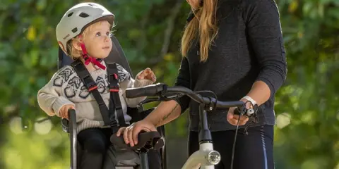 Kobieta z dzieckiem w foteliku rowerowym, gotowi na wspólną przejażdżkę. To idealny fotelik rowerowy dla małych podróżników.