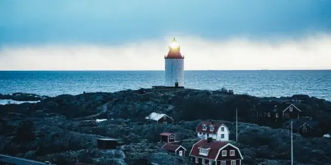 En fyr lyser över klippor och röda hus vid havet. En idyllisk plats för unika hotell Sverige.