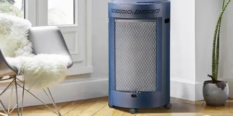 Un chauffage gaz infrarouge ou infrableu bleu, cylindrique et sur roulettes, diffuse sa chaleur dans un salon cosy, près d'un fauteuil confortable.