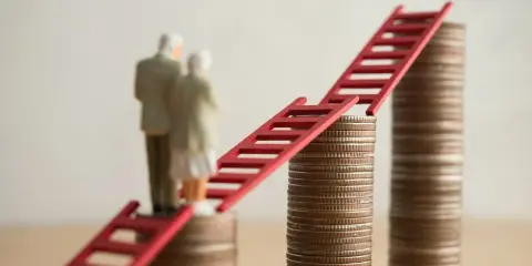 Figurki starszej pary stoją na stosach monet, połączonych czerwoną drabiną. Symbolizuje to nowe zasady przejścia na emeryturę i drogę do finansowej stabilności.