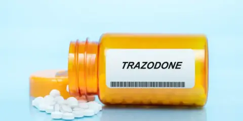 Pomarańczowa butelka z tabletkami trazodone neuraxpharm, kilka tabletek rozsypanych obok.