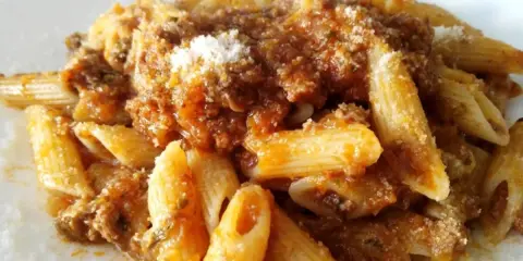 Penne al ragù di cinghiale, un piatto ricco e saporito, condito con abbondante sugo e una spolverata di parmigiano.
