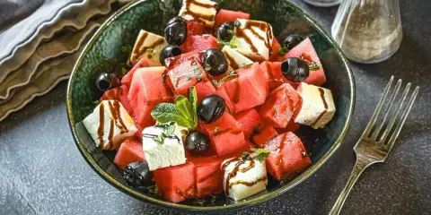 Erfrischender Melonen Feta Salat mit schwarzen Oliven und Minze, beträufelt mit Balsamico-Dressing. Perfekt für heiße Tage!