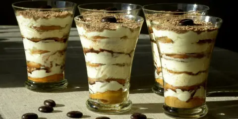 Pyszne tiramisu w pucharkach, warstwowo ułożone z kremem i biszkoptami, posypane czekoladą i kawą.