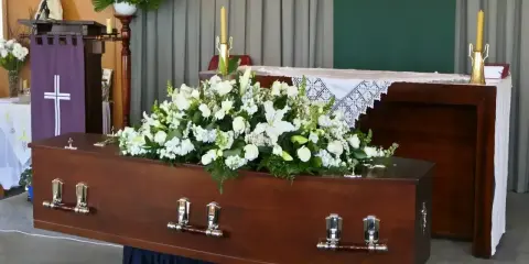 Drewniana trumna ozdobiona białymi kwiatami, przygotowana do świeckiego pogrzebu.