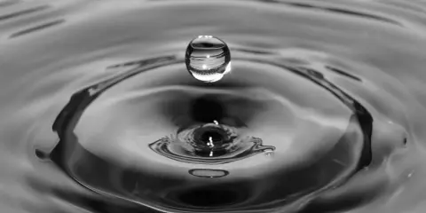 Goutte d'eau en suspension au-dessus de son impact, créant des ondulations. L'eau calcaire reflète la lumière.