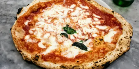 Pyszna pizza napoletana z rozpływającym się serem mozzarella i aromatycznym sosem pomidorowym, ozdobiona świeżą bazylią.
