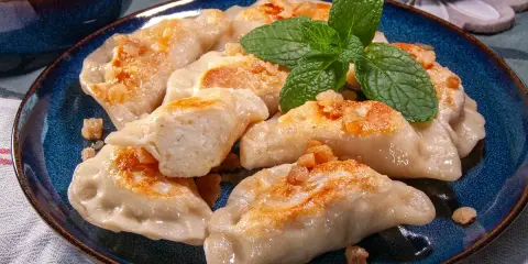 Pyszne pierogi ruskie przepis na talerzu, posypane skwarkami i udekorowane miętą.