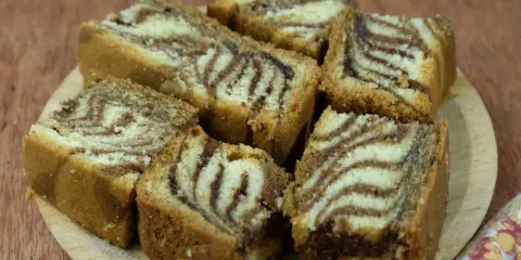 Kawałki ciasta zebra ułożone na drewnianej desce, z charakterystycznymi pasami jasnego i ciemnego ciasta.