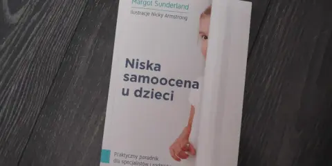 Książka "Niska samoocena u dzieci" Margot Sunderland. Na okładce fragment twarzy dziecka ukrywającego się za białą zasłoną.