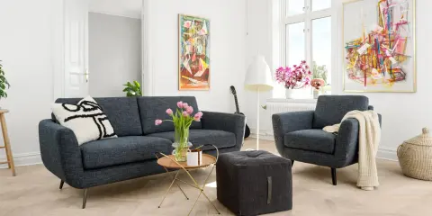 En modern soffgrupp 3+2 i mörkblått tyg, med en fåtölj, soffbord, pall och konst på väggarna.