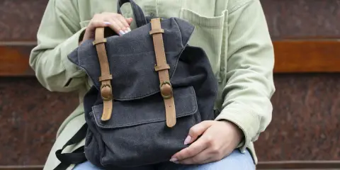 Osoba trzyma ciemnoszary plecak DIY z brązowymi skórzanymi paskami i klamrami.