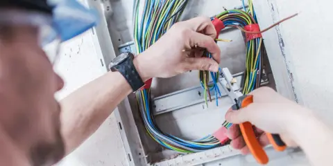 Elektryk pracuje nad prostą instalacją elektryczną, przycinając kolorowe przewody w skrzynce rozdzielczej.