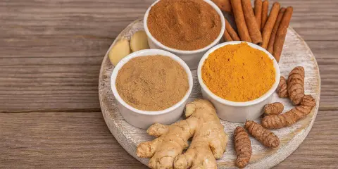 Poudre de curcuma, gingembre frais et bâtons de cannelle sur une planche en bois. Idéal pour un thé réconfortant au curcuma et miel.
