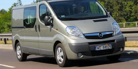 Srebrny Opel Vivaro 2.0 CDTI z przyciemnianymi szybami jedzie po drodze, otoczony zielenią.