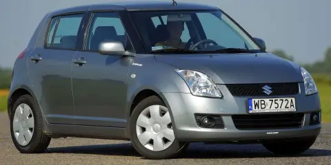 Szary Suzuki Swift 2007 z kierowcą za kierownicą, zaparkowany na drodze.
