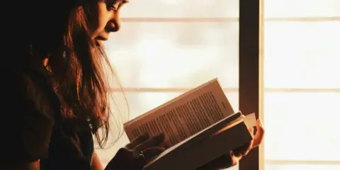 Ragazza immersa nella lettura, illuminata dalla luce dorata del tramonto, sfoglia pagine che potrebbero contenere i libri di Emmanuel Carrère.