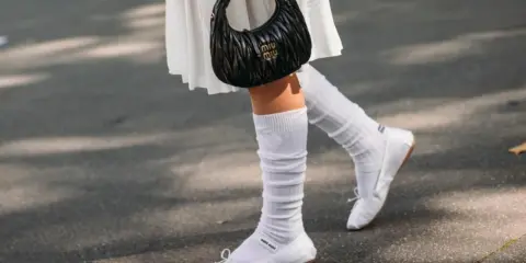 Piernas con bailarinas blancas y calcetines blancos arrugados, un look chic para bailarinas con calcetines.