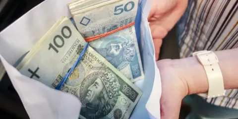 Koperta z plikiem banknotów 100 i 50 zł. Ile dać na 50 urodziny? Tyle pieniędzy to dobry prezent!
